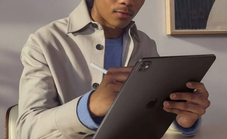 Gros plan d'une tablette noire tenue et utilisée avec un stylet blanc. Un manteau beige est visible.
