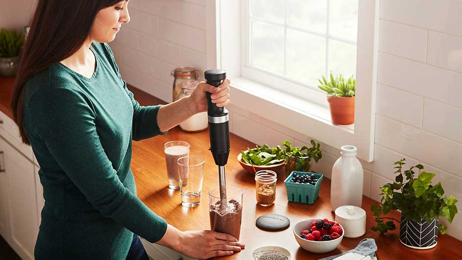 Een keukenopstelling met een blender in een glas, omringd door fruit, groenten en glazen op een houten aanrecht.