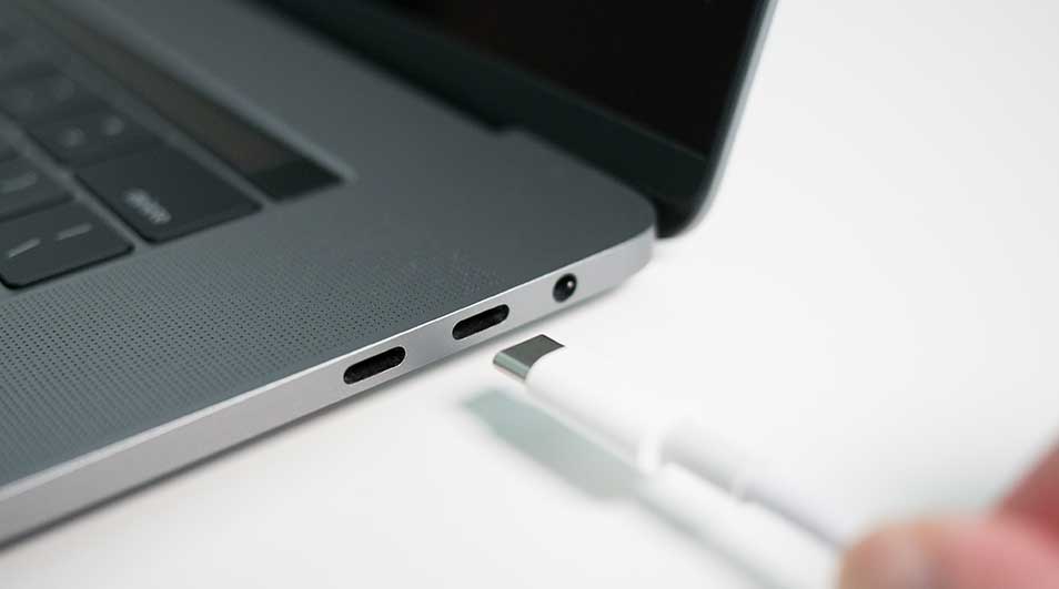 Een grijze laptop met een witte USB-C kabel die wordt aangesloten op een van de poorten, liggend op een wit oppervlak.