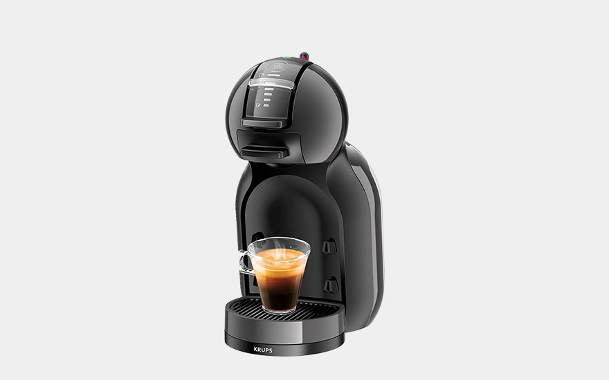 Een zilveren Nespresso-apparaat met een glas espresso, een doos en capsules in bruin, goud en paars.
