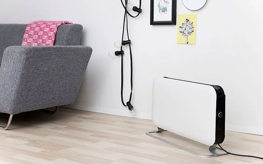 Grijze sofa met roze plaid, witte radiator en zwarte kabel tegen een witte muur op een houten vloer.