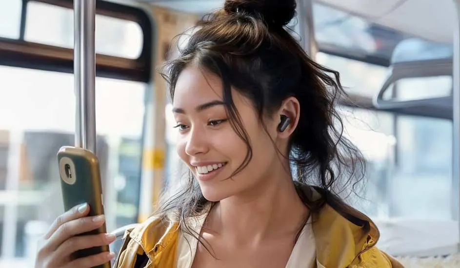 Une personne dans un bus tient un smartphone vert olive. Elle porte des écouteurs noirs. La lumière du jour entre par la fenêtre.