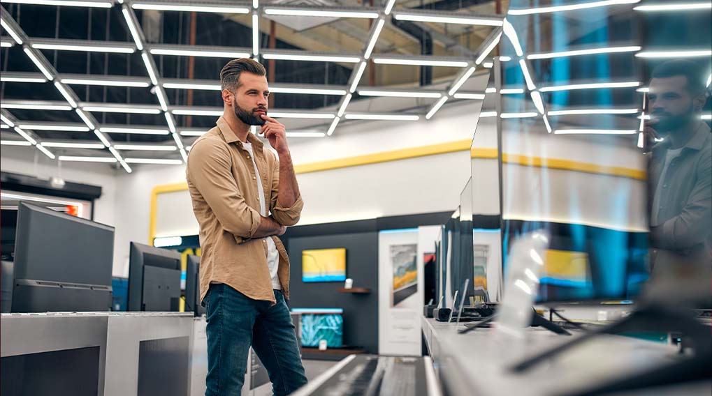 Een winkel met televisietoestellen, verlicht door een raster van lampen aan het plafond. Verschillende schermen staan op een rij.