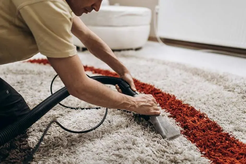 Gros plan sur le nettoyage d'un tapis à rayures orange et crème avec un appareil à buse grise et un tuyau noir.