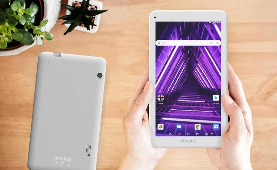 Tablette blanche avec écran violet tenue dans les mains, une autre tablette à côté, pots de plantes.