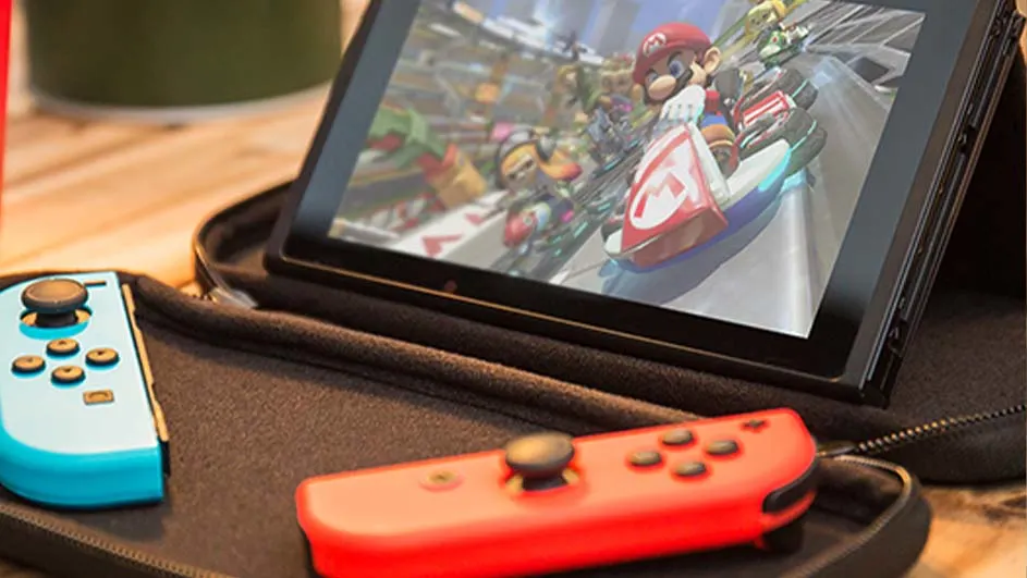 Une console de jeu affiche une course. Une manette rouge et une bleue sont posées à côté.
