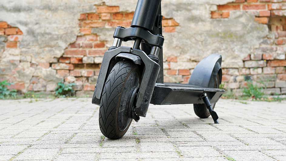 Een zwarte elektrische step staat op een betegelde ondergrond, met een bakstenen muur op de achtergrond.