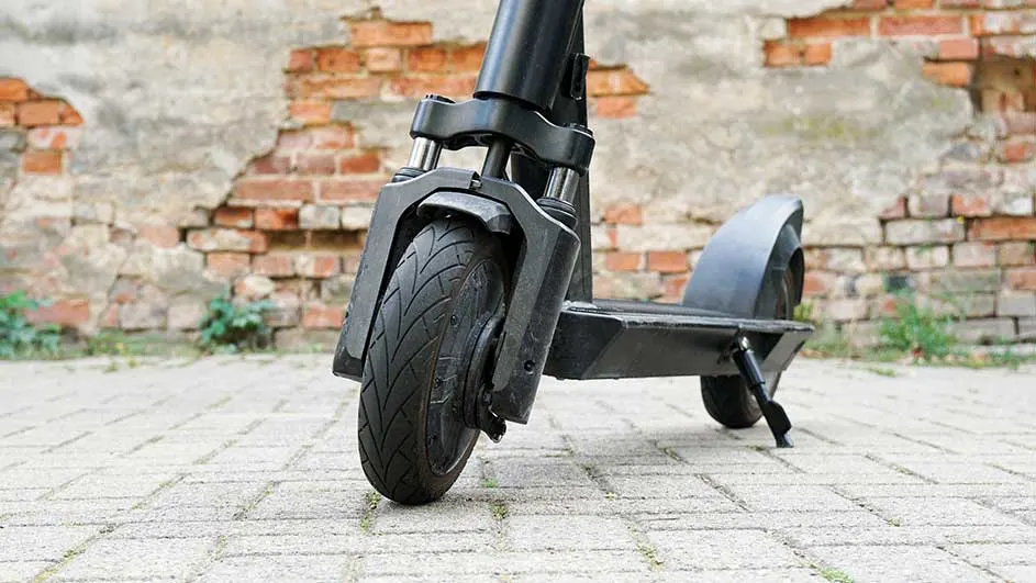 Een zwarte elektrische step staat op een betegelde ondergrond, met een bakstenen muur op de achtergrond.