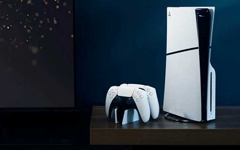 Console PlayStation 5 blanche avec deux manettes sans fil blanches sur un meuble en bois sombre.