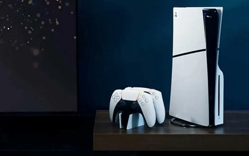 Console PlayStation 5 blanche avec deux manettes sans fil blanches sur un meuble en bois sombre.
