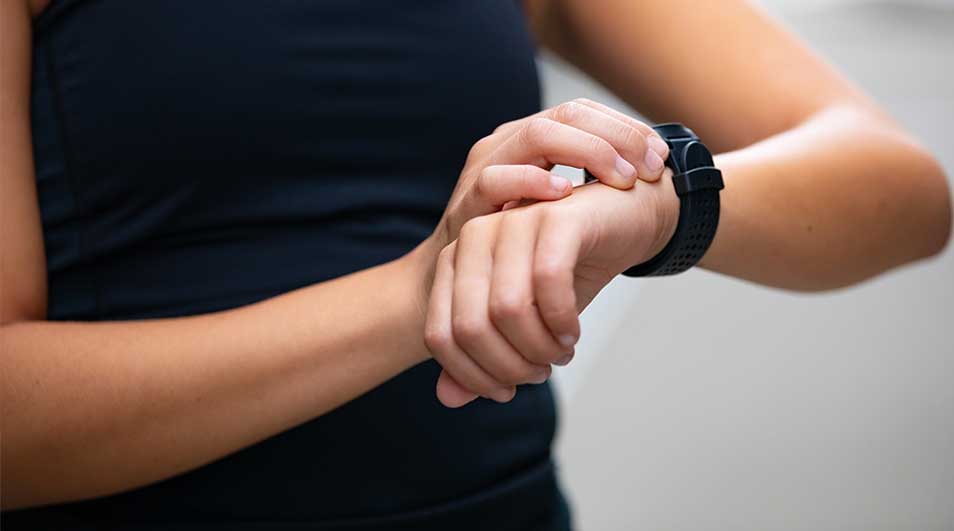 Iemand bedient of controleert een zwarte smartwatch om de pols, met focus op de handen en een neutrale achtergrond.
