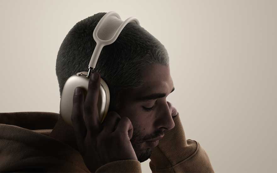 Side view of a person with closely shaved hair and hoodie wearing beige headphones, eyes shut, fully absorbed in music on a neutral background.