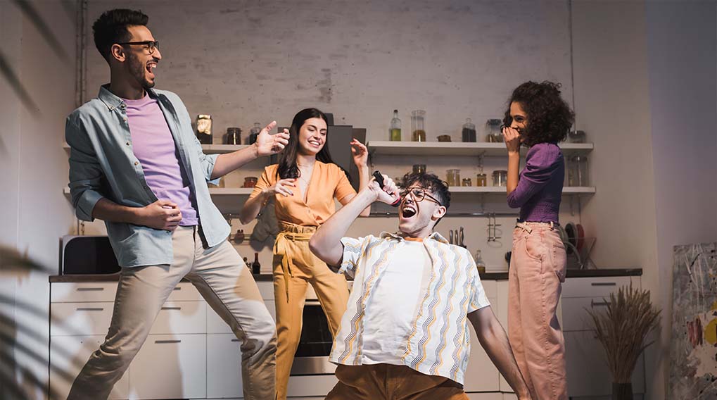 Een groep mensen staat in een keuken en doet alsof ze zingen en gitaar spelen.