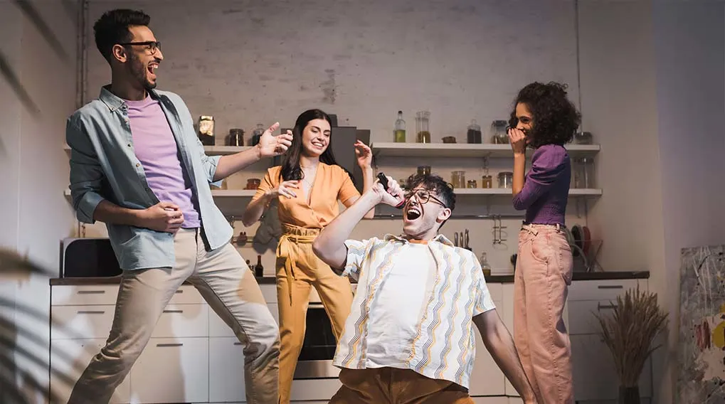 Een groep mensen staat in een keuken en doet alsof ze zingen en gitaar spelen.