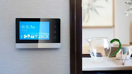 Écran tactile mural noir et argent affichant des icônes bleues, à côté d'une carafe transparente avec une poignée verte.