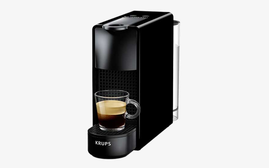 A slim black Krups coffee machine prepares an espresso in a glass cup, with a transparent water tank positioned at the back.