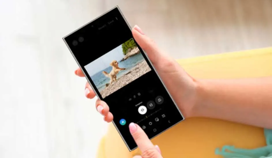 Une main tient un smartphone affichant une photo d'un chien sur une plage. L'interface de l'application est visible.
