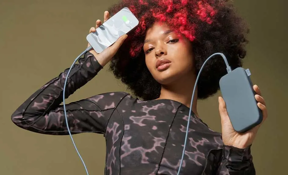 Een zilverkleurige telefoon is met een blauwe kabel verbonden met een blauwgrijze powerbank tegen een beige achtergrond.