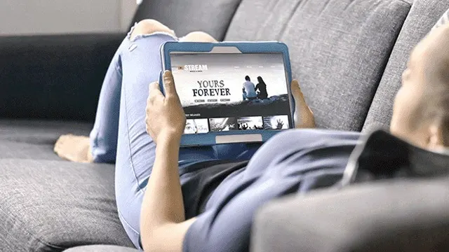 Sur un sofa gris, une tablette affiche "Yours Forever" avec des options de streaming.