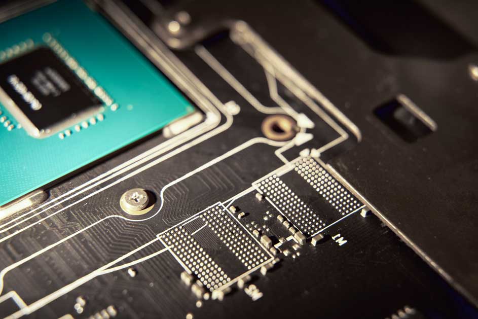 Detailopname van een zwarte printplaat met zilverkleurige circuits, een groene chip en kleine elektronische componenten.