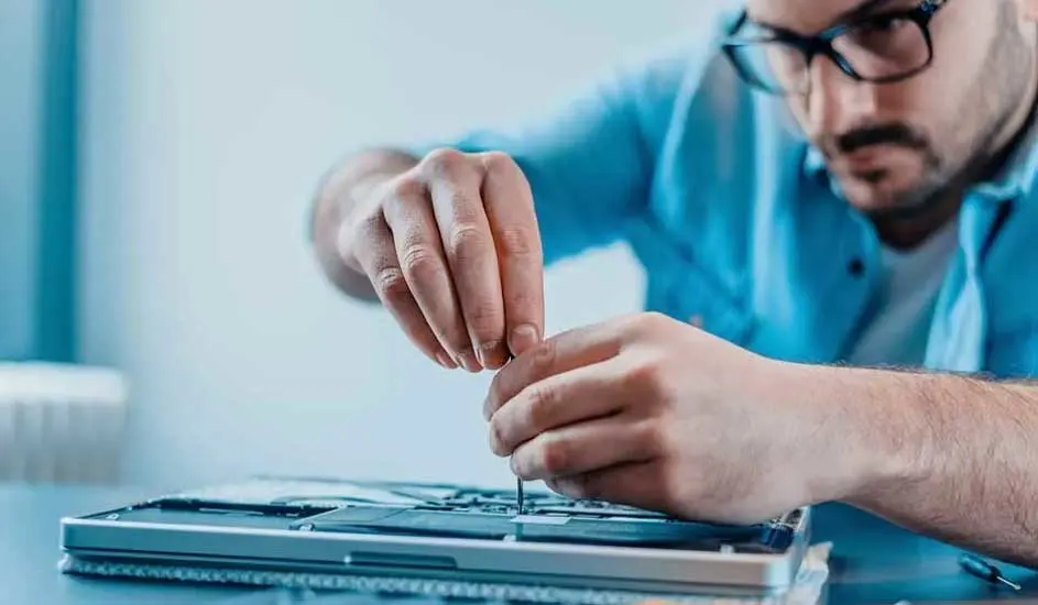 Een zilverkleurige laptop wordt gerepareerd met een schroevendraaier op een blauwe tafel tegen een blauwe achtergrond.