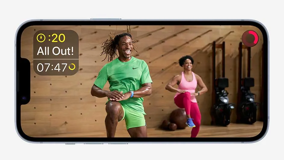 Un téléphone affiche une séance d'entraînement : homme en vert, femme en rose, et équipement sportif en arrière-plan.