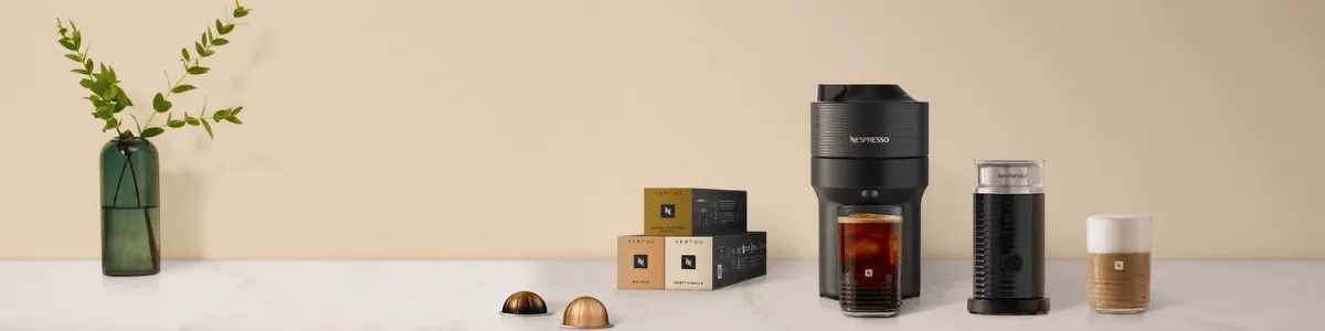 Machine Vertuo avec des capsules, un verre de café glacé et un mousseur à lait sur le plan de travail.