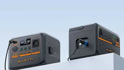 Twee zwarte BLUETTI powerstations met oranje details staan op een witte rand. Ze hebben meerdere aansluitingen en een modern ontwerp.