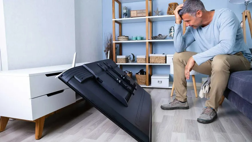 Een zwarte tv ligt op een houten vloer voor een witte kast. Een houten rek staat tegen een blauwe muur.