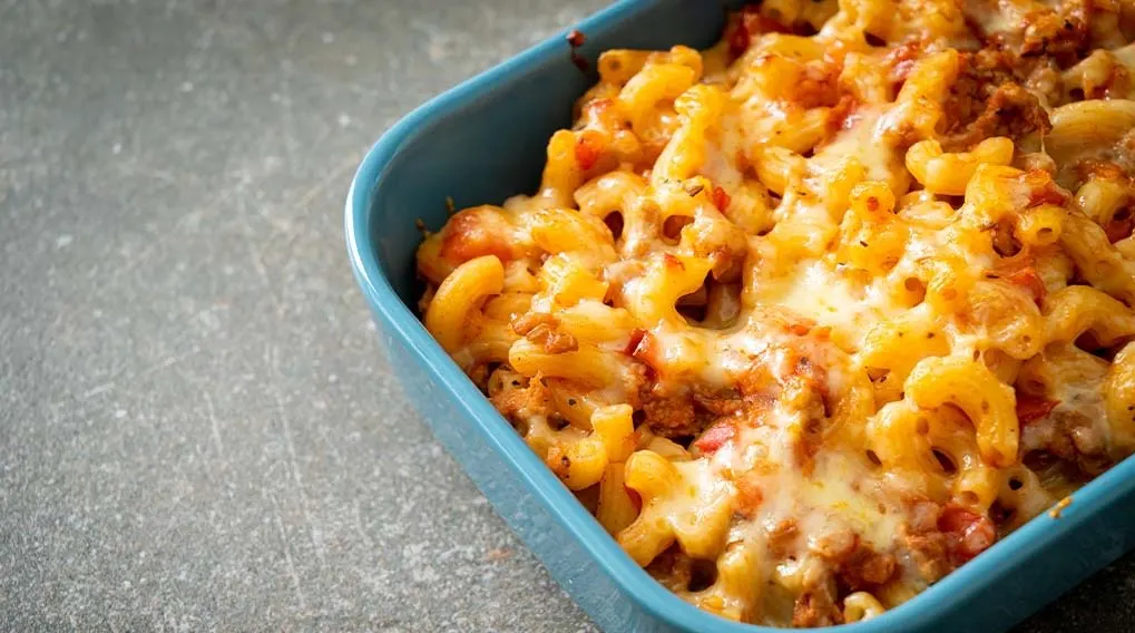 Een blauwe schaal gevuld met macaroni en kaas, met een gesmolten kaaslaag bovenop.