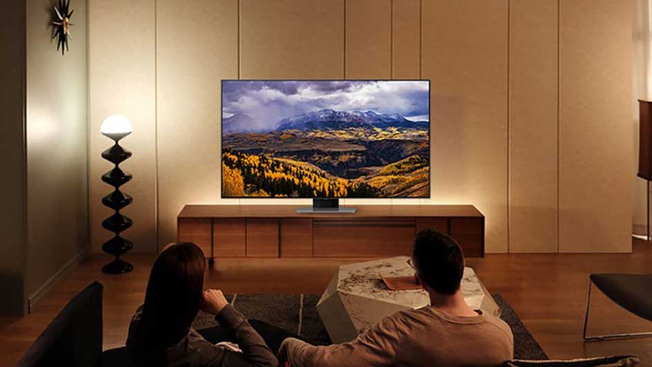 Salon avec TV montrant un paysage montagneux, meuble TV en bois, lampe design et table basse géométrique.