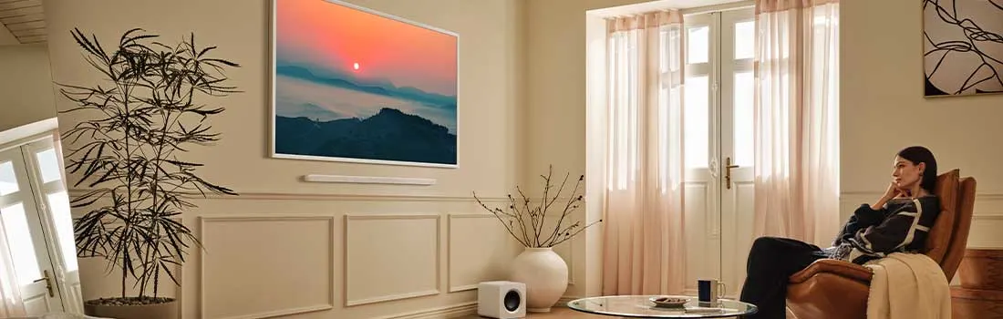 Une femme est assise confortablement dans un salon lumineux et regarde un tableau coloré représentant un coucher de soleil au mur.