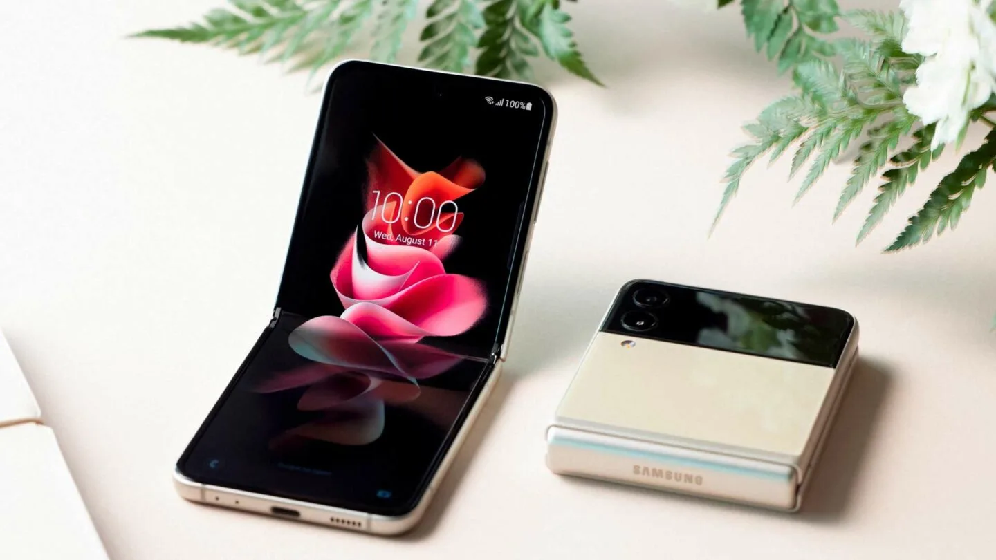 Deux smartphones pliables sur une surface blanche avec des fleurs. Un téléphone est ouvert, affichant l'heure 10:00 sur un écran.