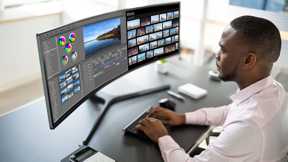 Un écran large affiche un logiciel de montage vidéo avec des images et des outils de couleur. Un clavier et une souris sont sur le bureau.