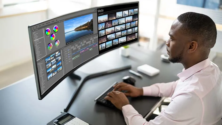 Un écran large affiche un logiciel de montage vidéo avec des images et des outils de couleur. Un clavier et une souris sont sur le bureau.