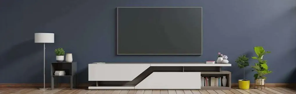 Une pièce avec un mur bleu, une télé, un meuble TV blanc, une lampe et des plantes.