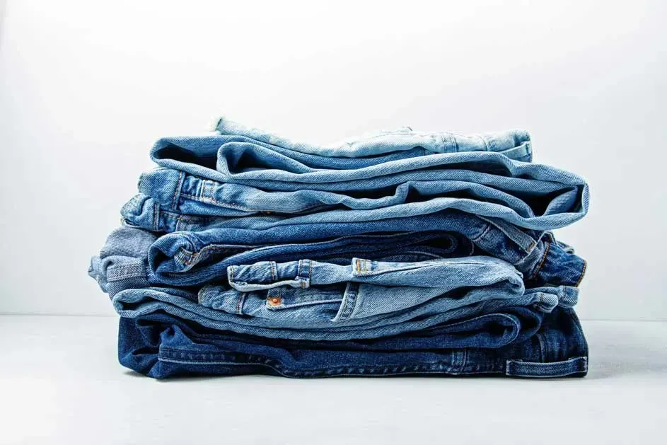 Pile de jeans bleus délavés et foncés sur fond blanc.
