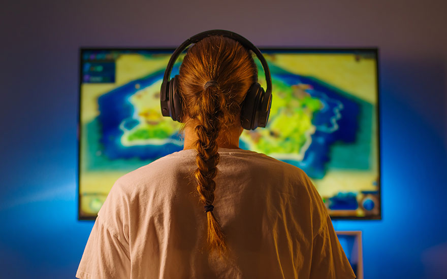 Vue arrière d'une personne avec un casque audio devant un écran affichant un jeu vidéo aux couleurs vives.