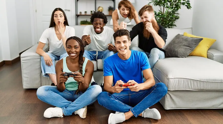 Een woonkamer met een witte bank, houten vloer en zes mensen die videogames spelen met gamecontrollers.