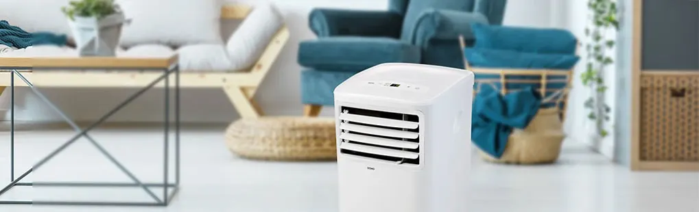 Domo mobiele airconditioner staat in een lichte, moderne woonkamer met een bank, fauteuil en planten; merk Domo goed zichtbaar.