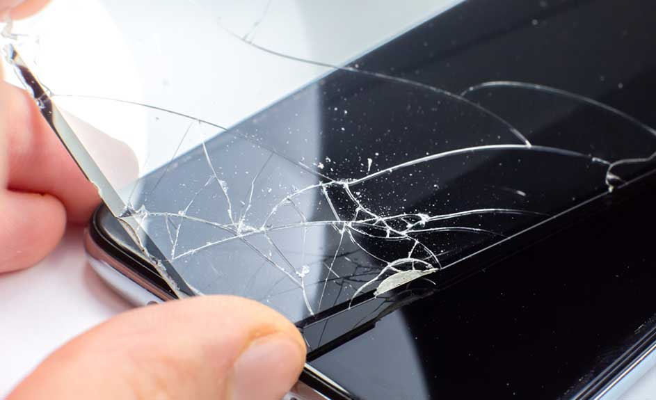 Zwarte smartphone met gebarsten scherm wordt door een hand vastgehouden, tegen een witte achtergrond.