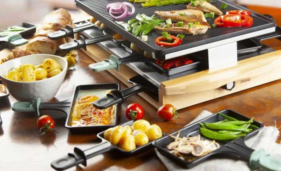 Une raclette avec des légumes, de la viande et du fromage. Des pommes de terre et du pain sont aussi sur la table.