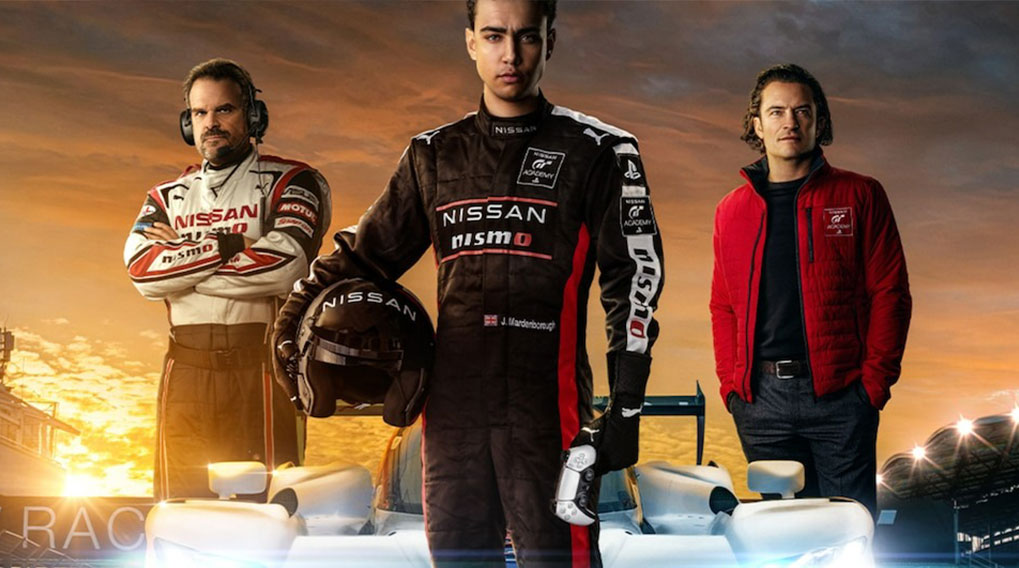 Drie personen in racekleding staan voor witte raceauto's op een circuit bij zonsondergang.