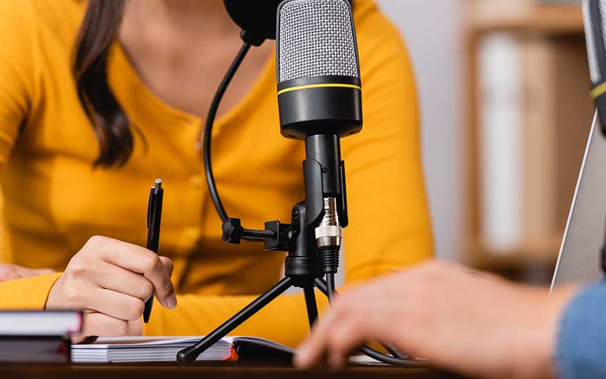 Microphone noir sur trépied sur une table en bois avec des livres et un stylo. Arrière-plan flou.