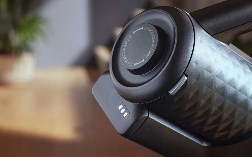Gros plan sur un aspirateur noir avec un filtre rond et des indicateurs de batterie sur une surface en bois.