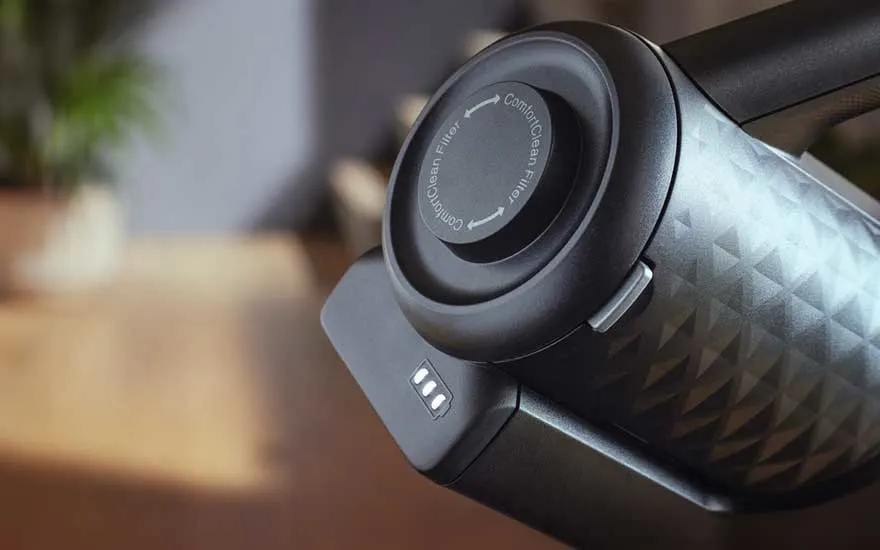Gros plan sur un aspirateur noir avec un filtre rond et des indicateurs de batterie sur une surface en bois.