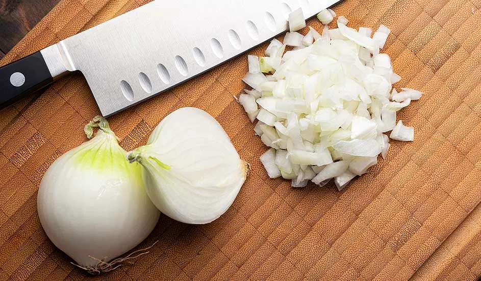 Sur une planche à découper en bois, un couteau, deux oignons entiers et un tas d'oignons hachés.