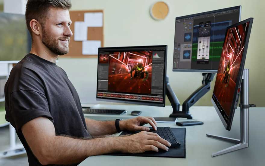 Een bureau met drie computerschermen die beelden van een computerspel tonen, een zwart toetsenbord en een muismat.