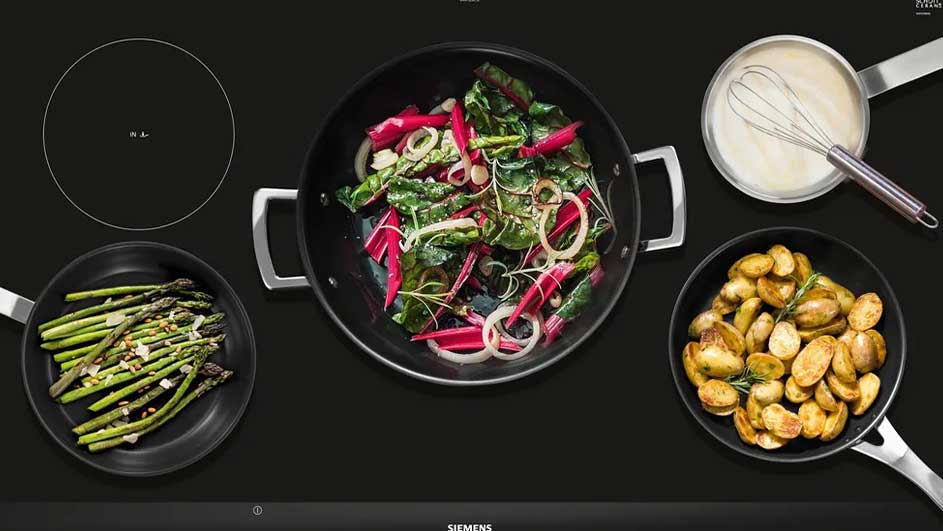 Vue de dessus d'une plaque de cuisson noire avec légumes, pommes de terre et sauce dans des casseroles.