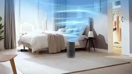 Chambre claire avec lit double, table de chevet et purificateur d'air. Des rideaux et une fenêtre laissent entrer la lumière du jour.